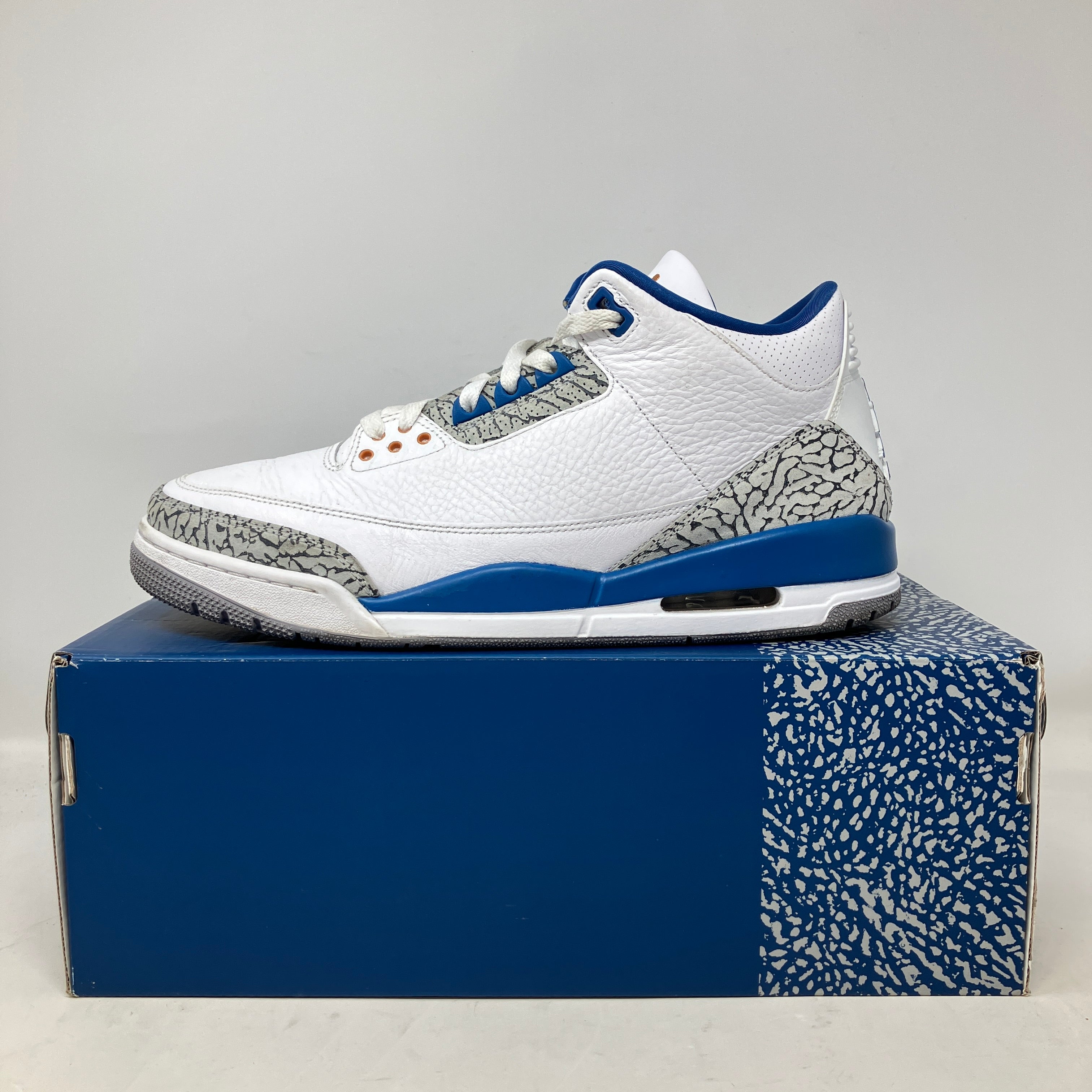 Side view of pre-owned white and blue Jordan 3 Retro Wizards sneaker on its original box with elephant print detailing