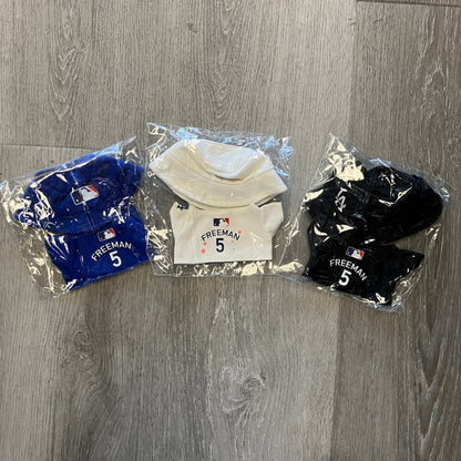 Set of black, blue, and white Freddie Freeman Labubu Dodger jerseys in packaging on wooden floor