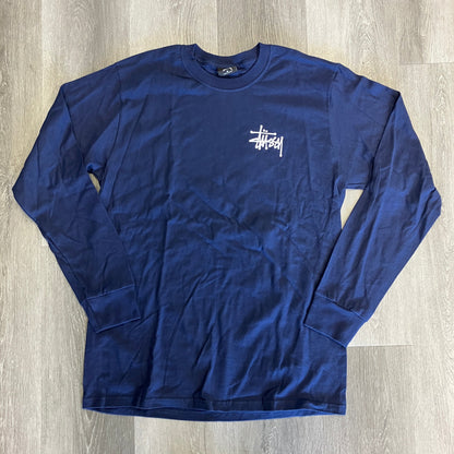 Navy Stussy Long Sleeve Tee with white logo, brand new, laid flat on wooden floor