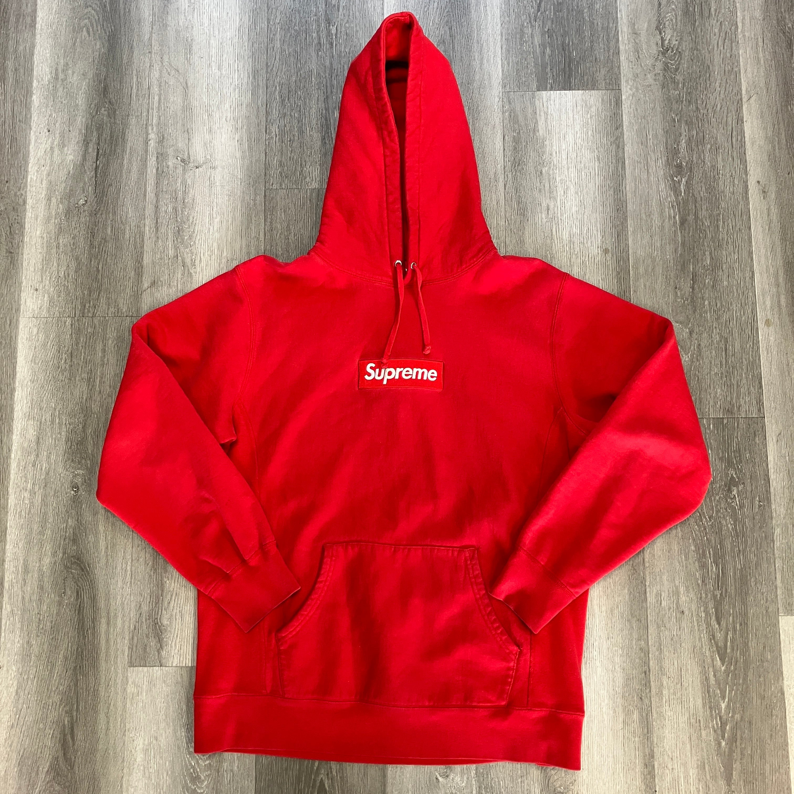 Red Supreme Box Logo hooded sweatshirt laid flat on wooden floor, pre-owned condition.