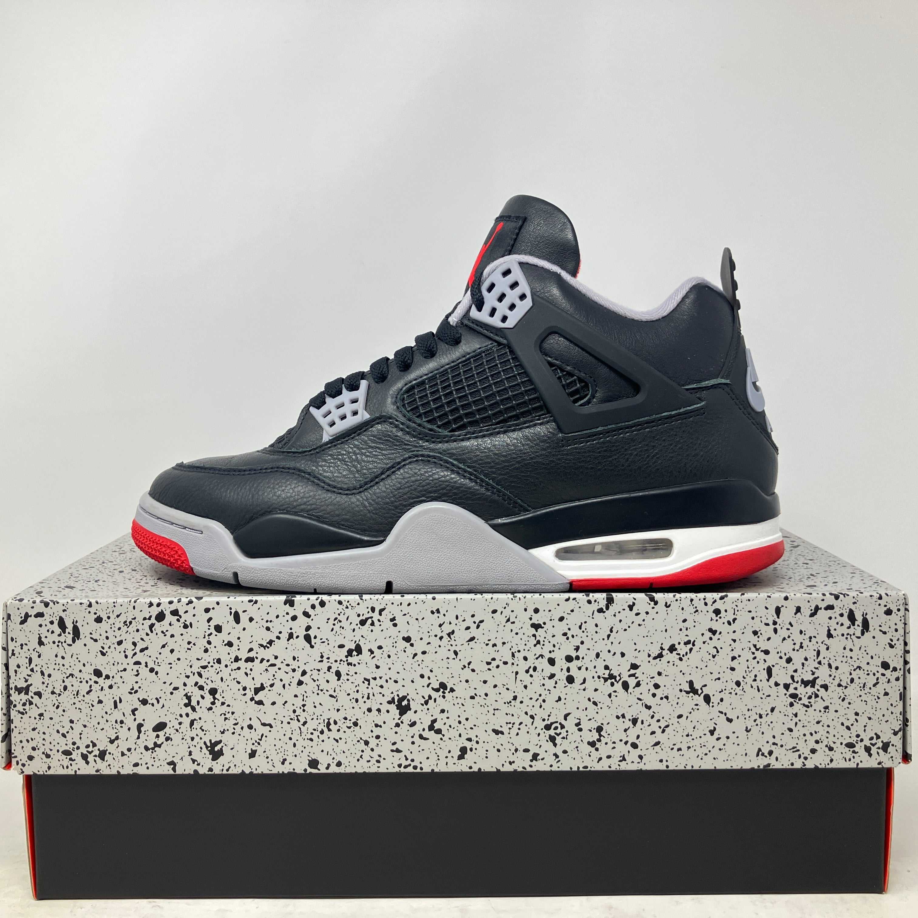 Black and red Jordan 4 Retro Bred Reimagined sneaker on speckled box, pre-owned with accessories included
