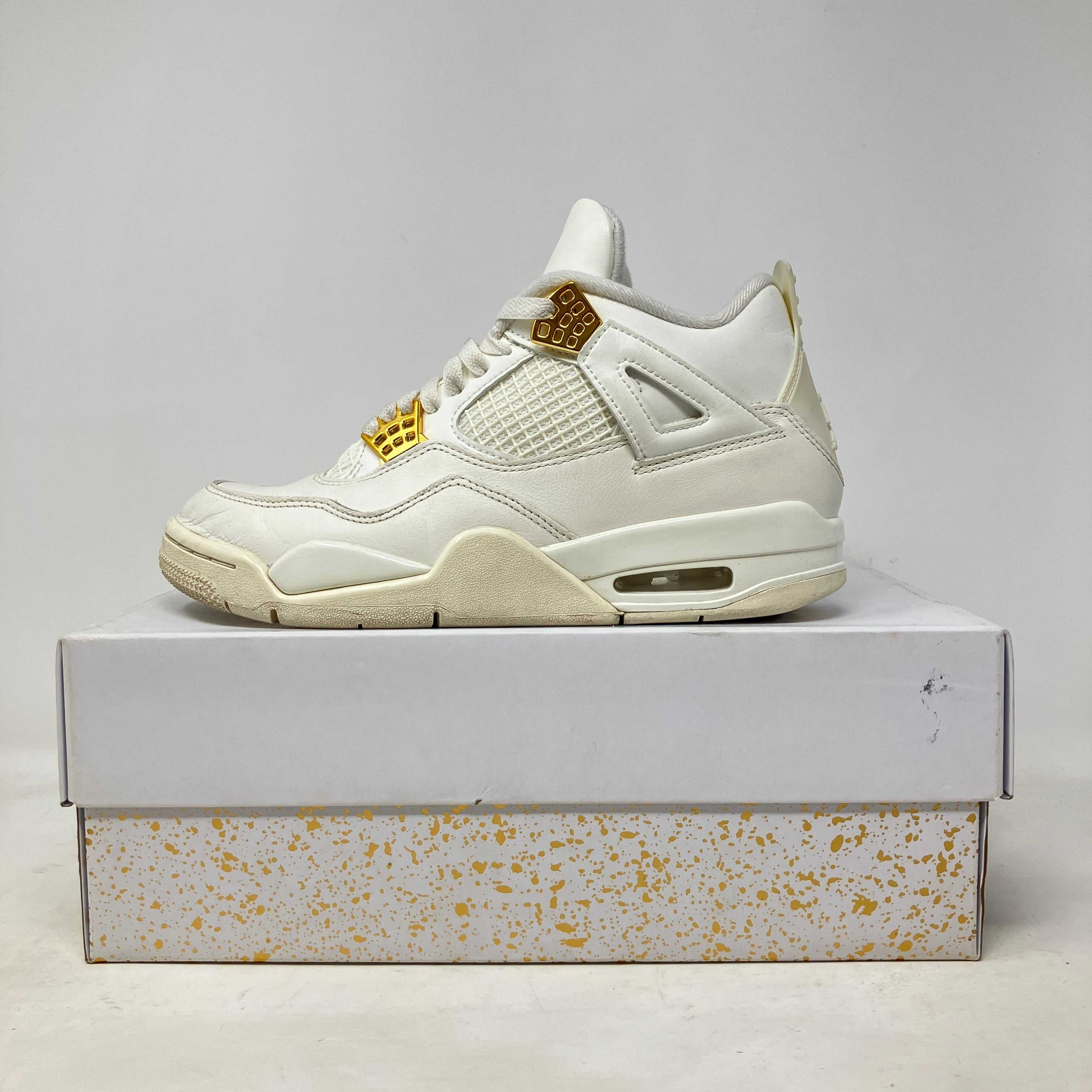 Jordan 4 Retro Metallic Gold women's sneaker in pre-owned condition with gold accents on white, displayed on a white and gold-speckled box