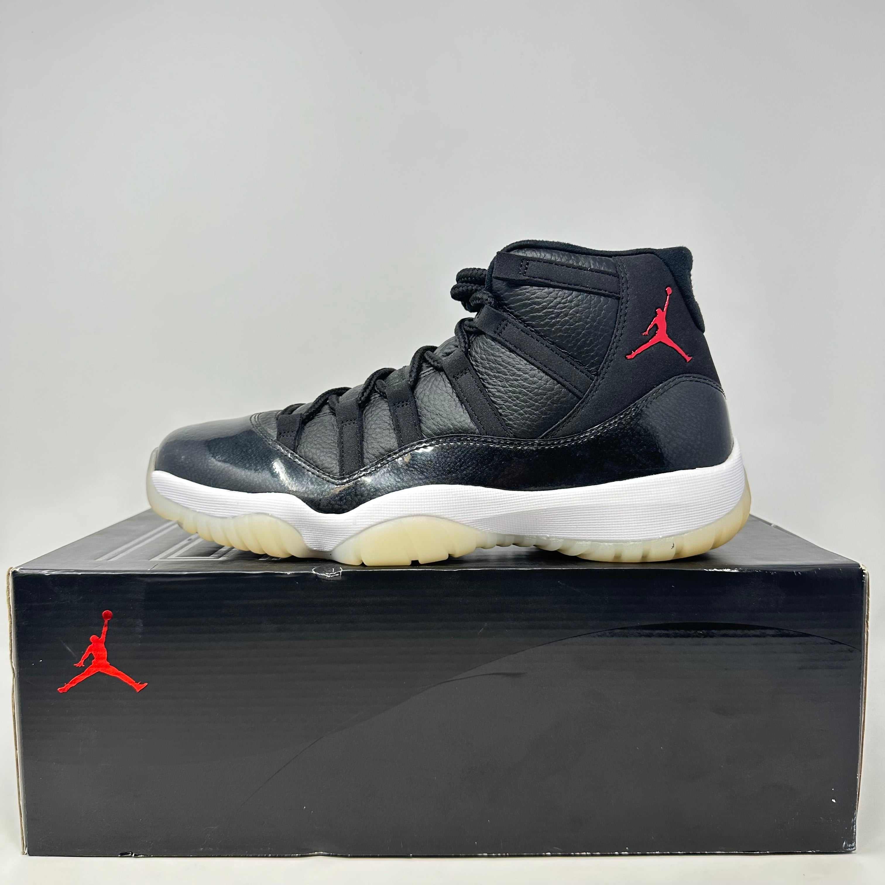 Jordan 11 Retro 72-10 black sneaker with red Jumpman logo on box and shoe, brand new condition with all accessories.