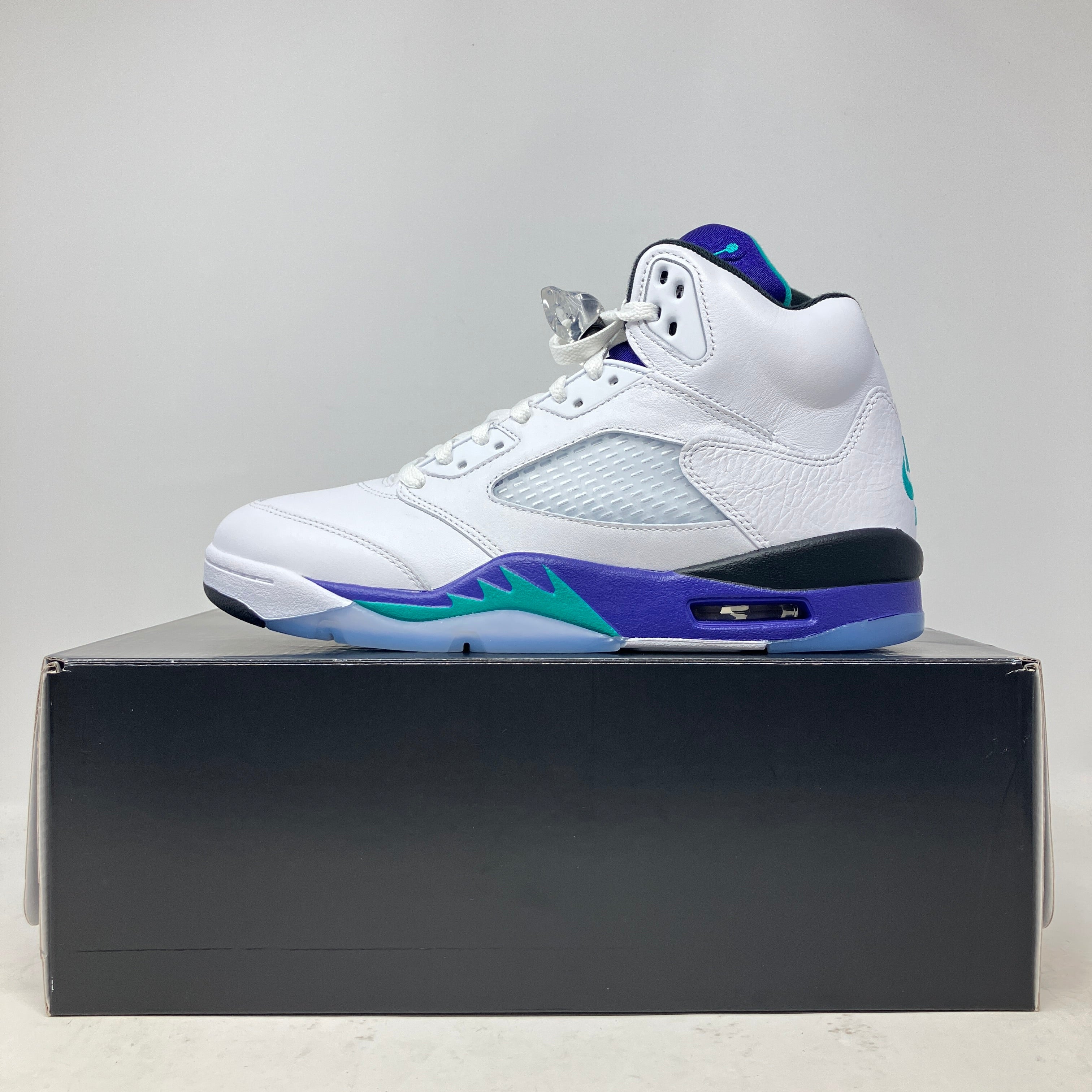 White and purple Jordan 5 Retro Grape sneaker displayed on black box, brand new with all accessories included