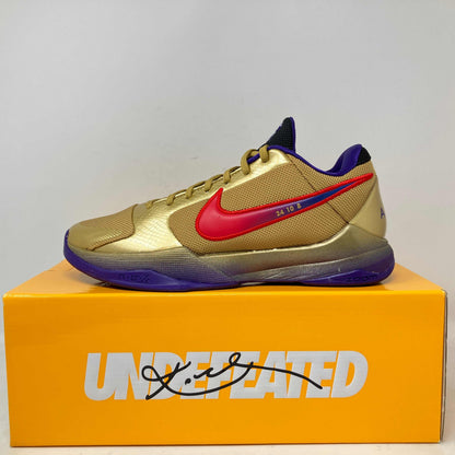 Nike Kobe 5 Protro basketball shoe in gold with red swoosh and purple accents on Undefeated branded box