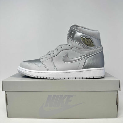 Jordan 1 Retro High sneaker in neutral grey leather with metallic accents, gold logo, and white sole on a grey Nike box.