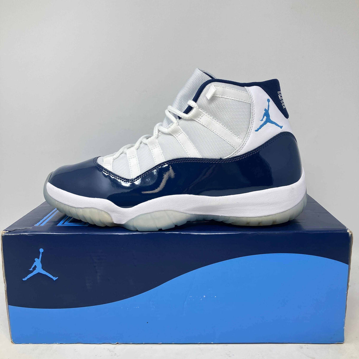 Jordan 11 Retro UNC basketball shoe in white and navy patent leather with a blue Jumpman logo and translucent sole on a matching box.