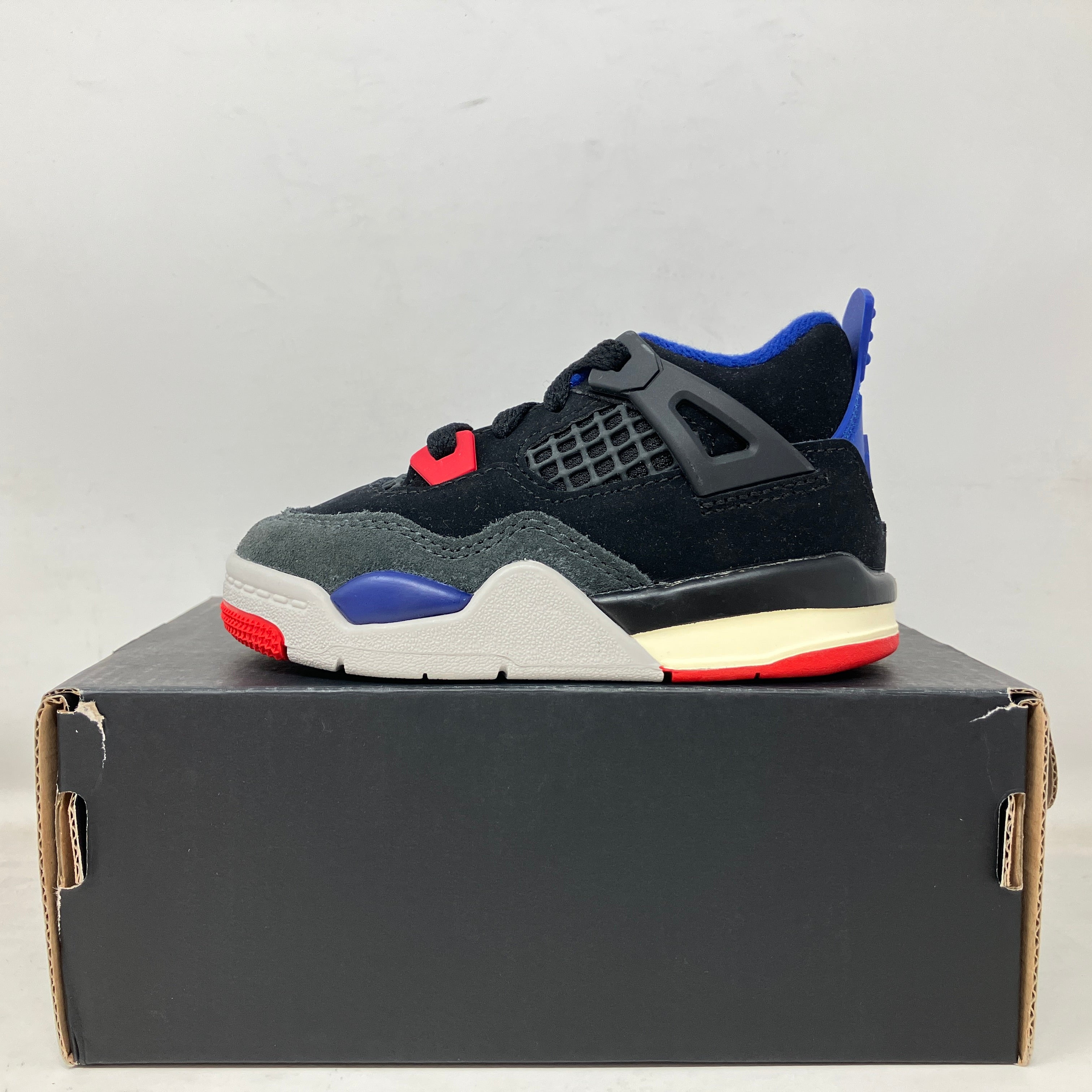 Black, blue, and red Jordan 4 Retro Rare Air toddler sneaker on black shoebox, brand new with all accessories included