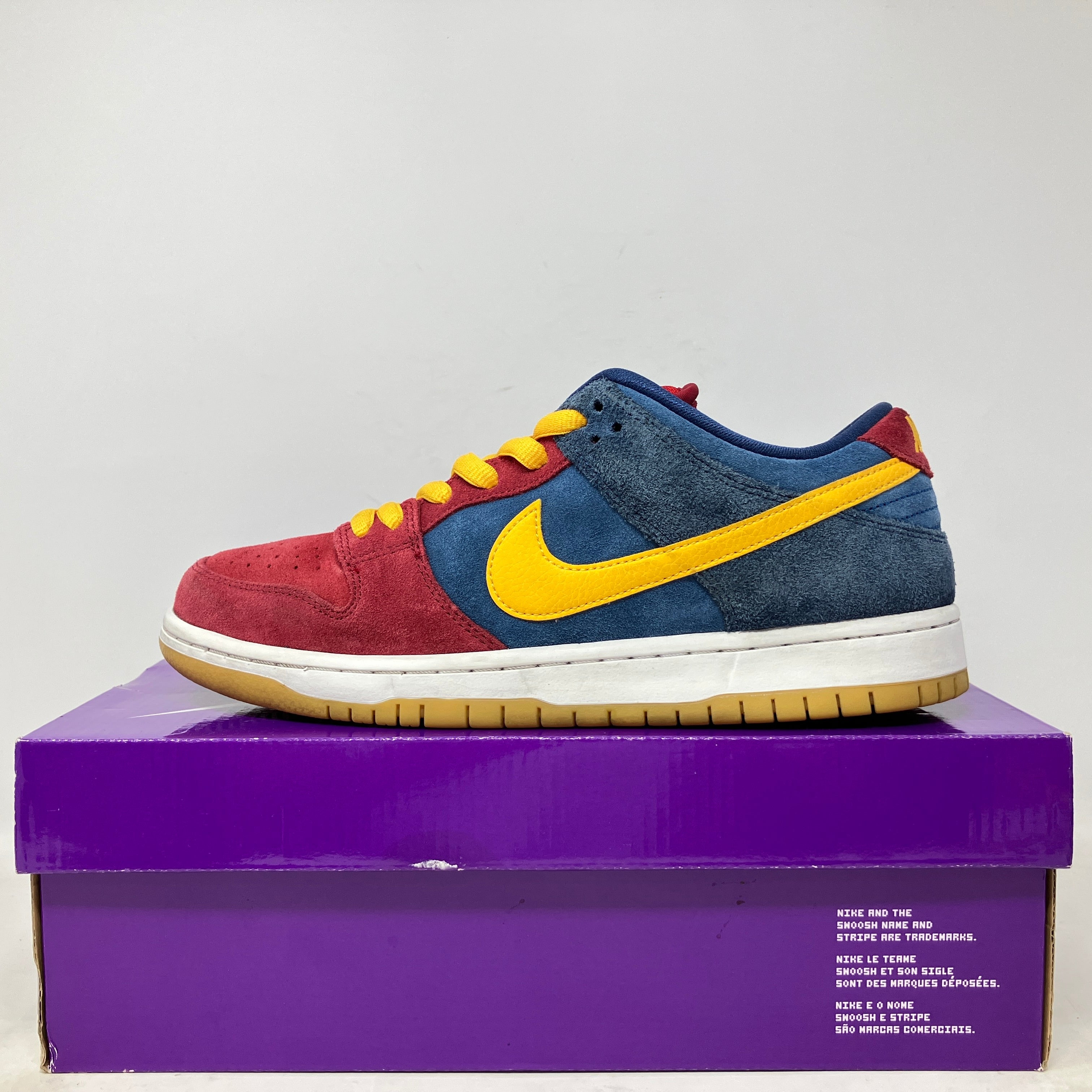 Nike SB Dunk Low Barcelona sneaker in red, blue, and yellow on purple box, pre-owned condition with accessories included