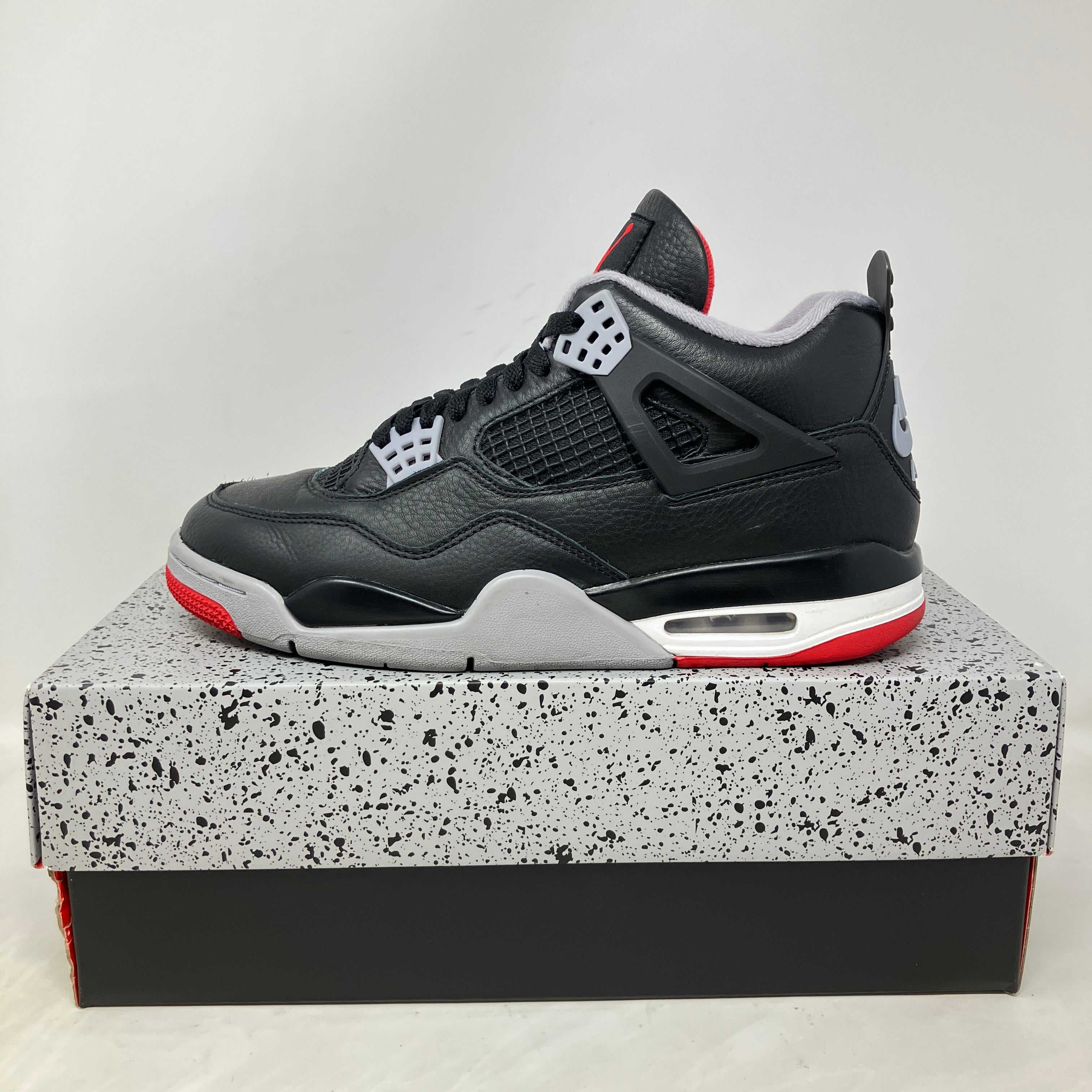 Jordan 4 Retro Bred Reimagined black and red sneaker on speckled box, pre-owned with accessories included