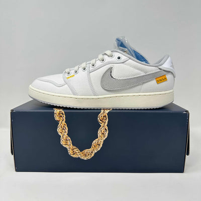 Jordan 1 Retro low-top sneaker in white canvas with a grey Swoosh, cream sole, yellow Union tag and exposed stitching.