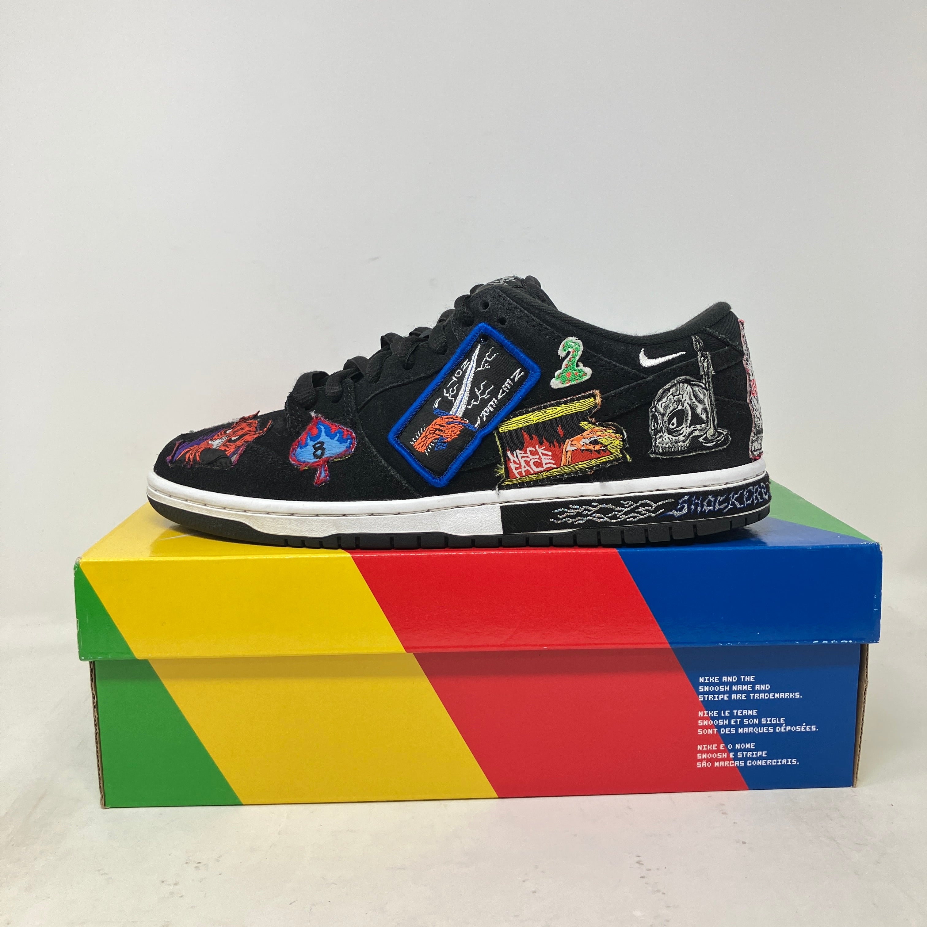 Nike SB Dunk Low Pro QS Neckface sneakers with colorful patches, pre-owned condition, on a multicolored box.