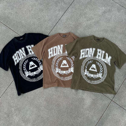 Three oversized Hidden Realm 'College' Tee shirts in black, brown, and olive green with white graphic print, laid flat on concrete.